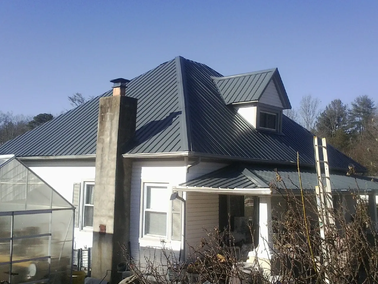 Dark blue standing seam metal roof on a white farmhouse with dormer — Slate & Tile Roof Repair by Roofing Brothers in Brodnax