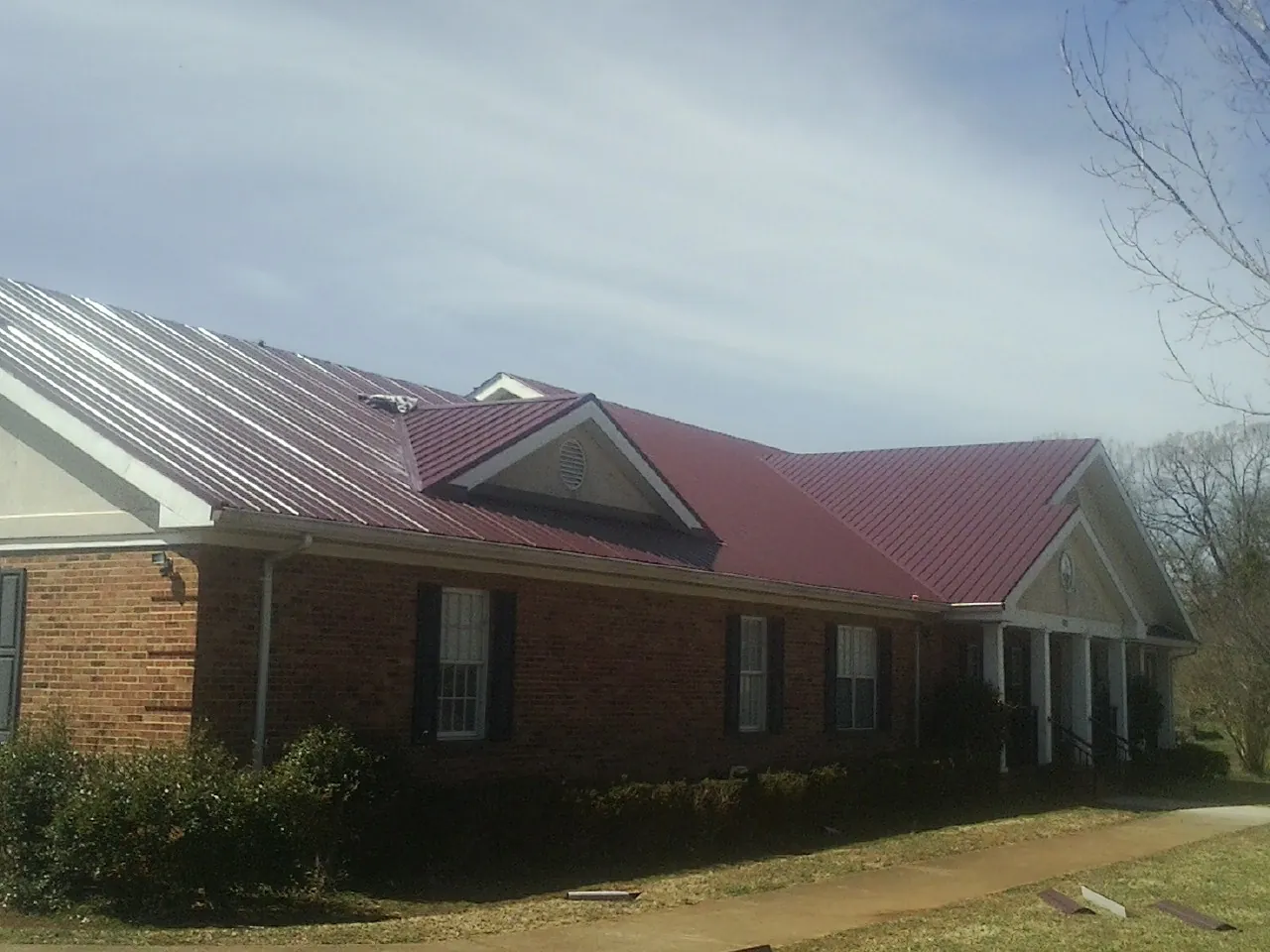 Red metal roof with gabled entries on a long brick building, from a Hail Damage Roof Repair job in Brodnax