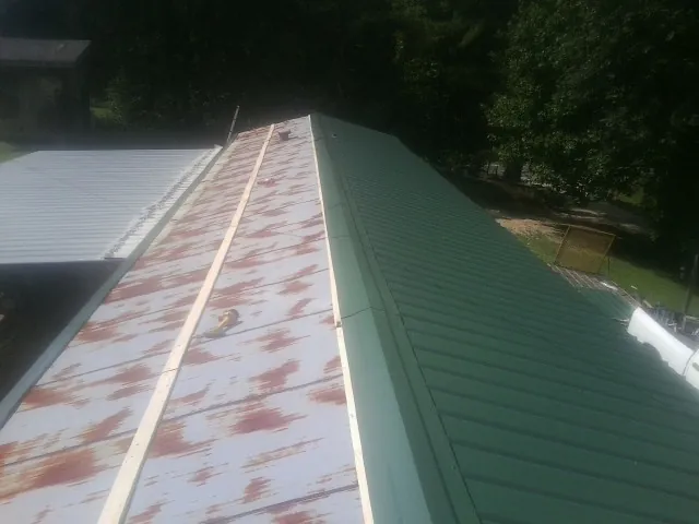 Old rusted panels beside newly installed green metal roofing — Wind Damage Roof Repair by Roofing Brothers in Brodnax