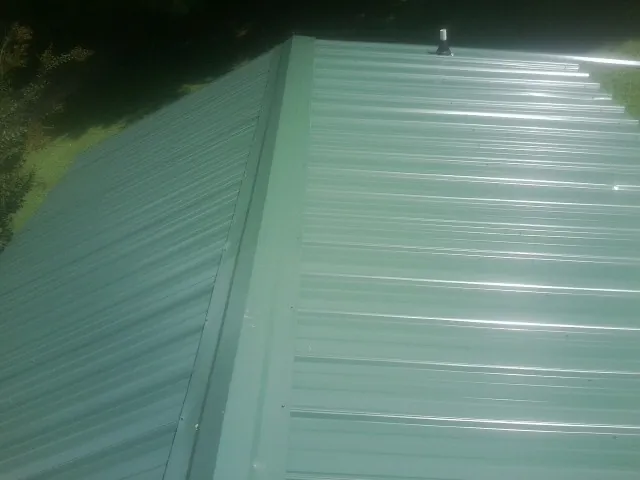 New green metal panels meeting at the ridge of a roof — Flat Roof Repair work by our crew in Brodnax
