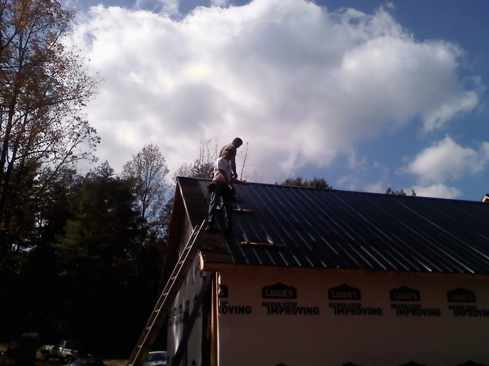 Roofer fastening dark metal panels high against a cloudy sky, from a Roof Inspection job in Brodnax