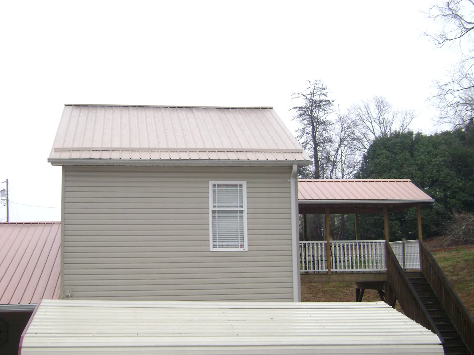 Tan metal roofs on a two story addition and attached porch, from a Roof Replacement job in Brodnax